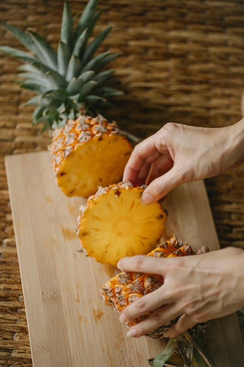 From above of unrecognizable female standing at table with ripe round piece of pineapple placed on cutting board in kitchen
