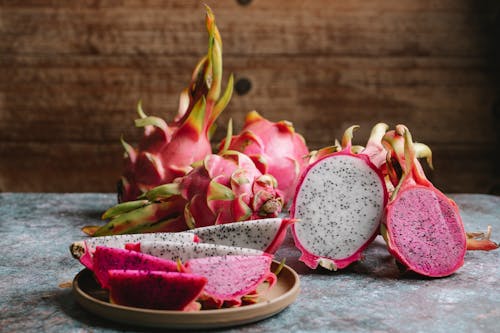 Ripe sliced dragon fruit with colorful flesh served on plate and placed on gray table against wooden wall in kitchen