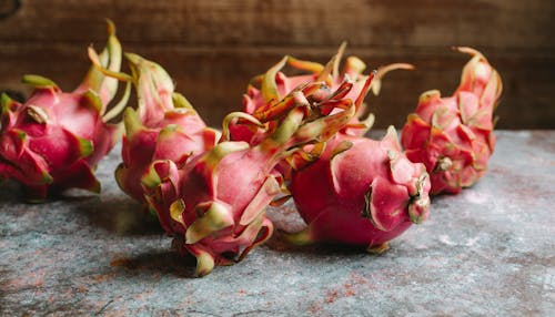 Heap of whole ripe tasty dragon fruits with pink peel placed on marble surface against wooden wall in light kitchen