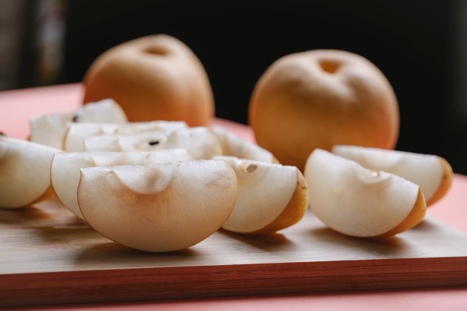 Whole and quartered Korean/Asian pears on a wooden board, showing the pale flesh used in bulgogi marinade