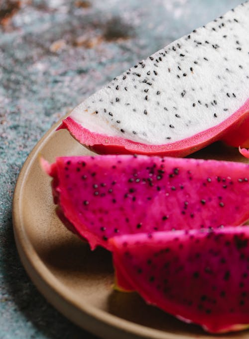 Pieces of ripe tasty dragon fruit with pink and white flesh served on round plate on marble table in kitchen