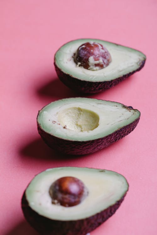 Sliced ripe organic avocados with seeds and green soft flash arranged in even row on pink background in bright studio