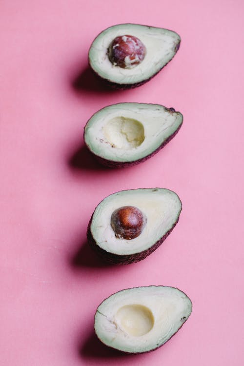 Composition of ripe sliced avocados with round seeds and green flesh arranged in even row on pink background in studio