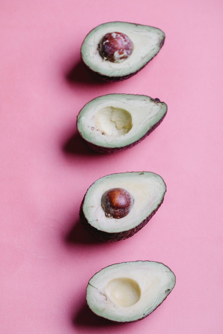 Row Of Halved Avocados On Pink Background