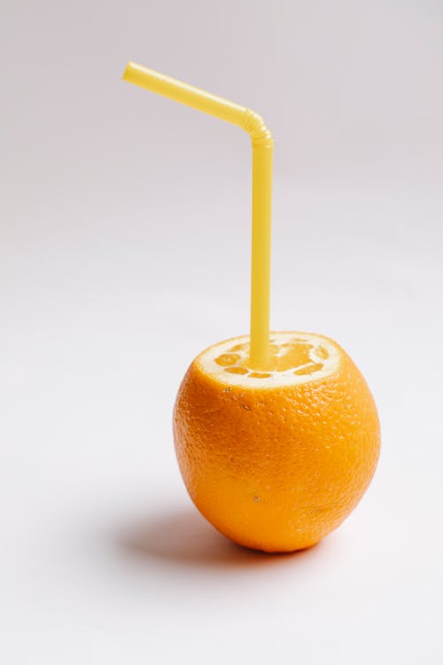 Cut fresh juicy ripe unpeeled orange with small yellow straw looking like glass with juice