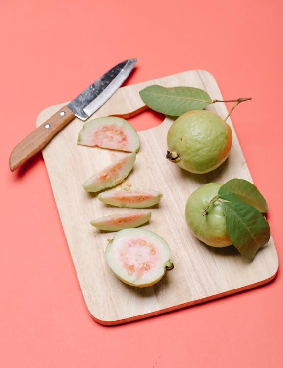 Top view of whole fruits of ripe fresh guava and cut in pieces on wooden cutting board on pink background