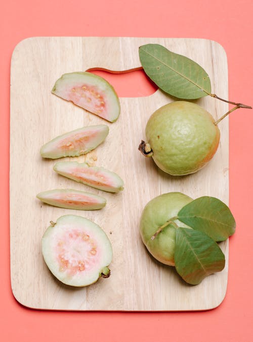 Top view of whole ripe fresh fruits of guava with leaves and cut in pieces on wooden cutting board on pink surface