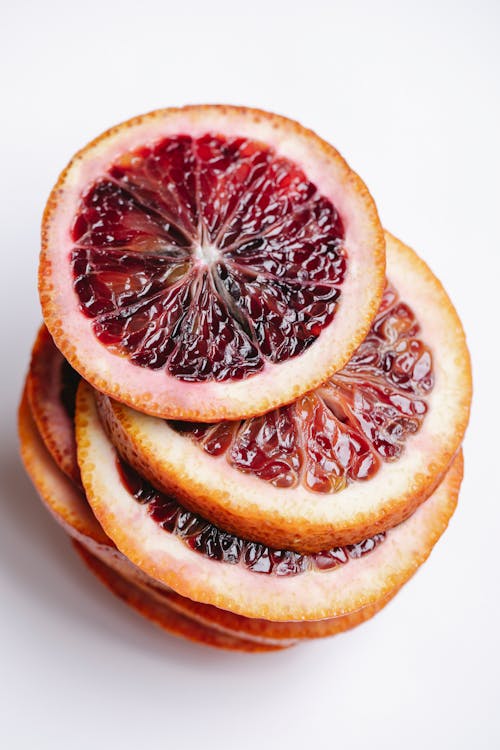 From above of heap of unpeeled fresh ripe juicy red orange slices on white background