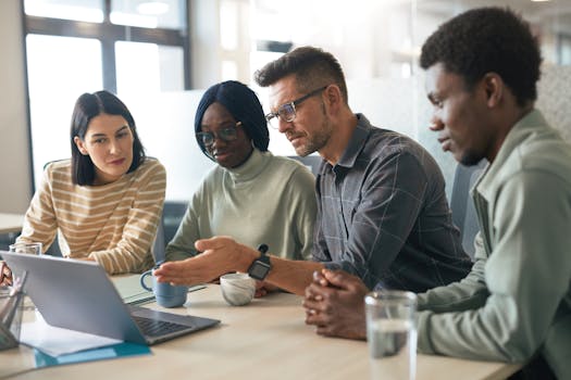 A diverse group of colleagues discussing work around a laptop in a modern office.