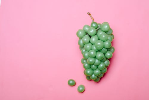 Ripe fresh green grapes on pink surface