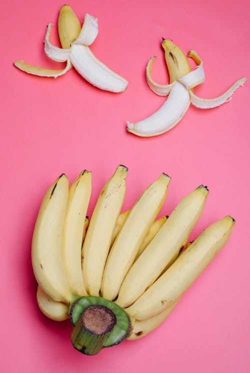 Top view of tasty half peeled and big hand of unpeeled bananas on pink background