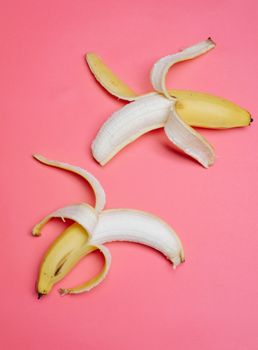 将两个部分去皮的成熟香蕉放在鲜艳的粉红色背景上，采用俯视图