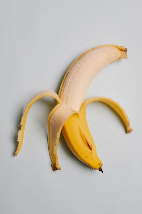 From above of half peeled ripe fresh tasty banana with yellow skin on white background