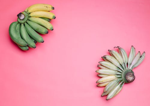 Hands of bananas on pink surface