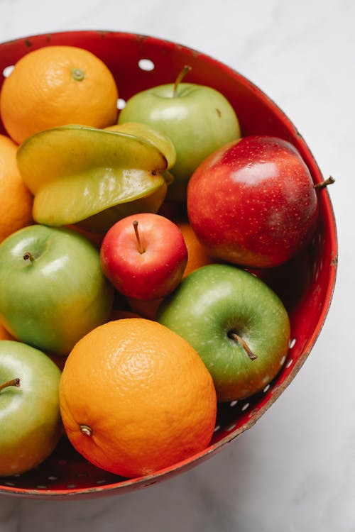Free From above of assorted ripe apples with juicy oranges and star fruit in colander Stock Photo