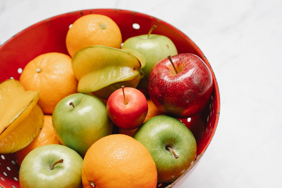 Assorted fresh apples and grapes in a red bowl on white background