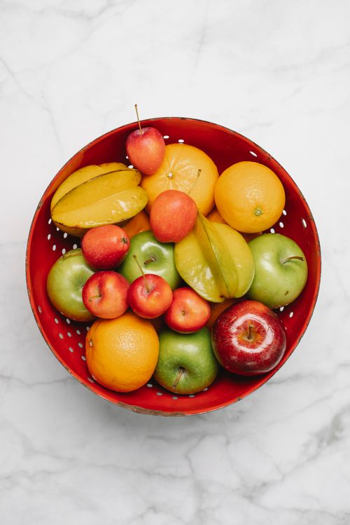 Free Top view of red bowl with fresh tasty fruits placed on white marble surface in light room Stock Photo