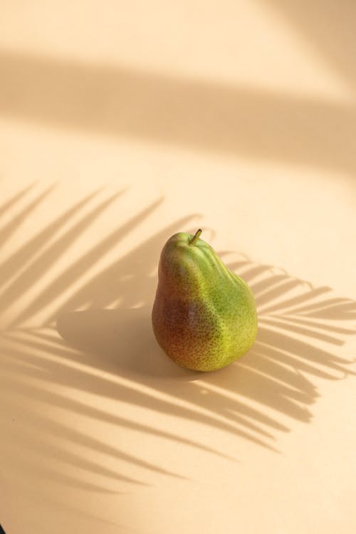 Ripe green and red fruit pear on white surface under palm branch