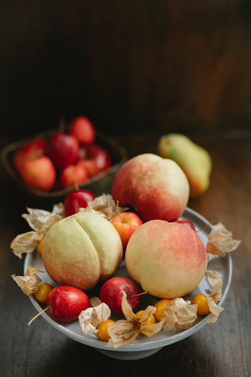 High angle of fresh ripe peaches with winter cherries and apples in bowl on table