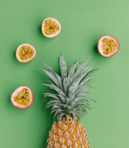 From above of composition of fresh pineapple with halves of passion fruit on green background