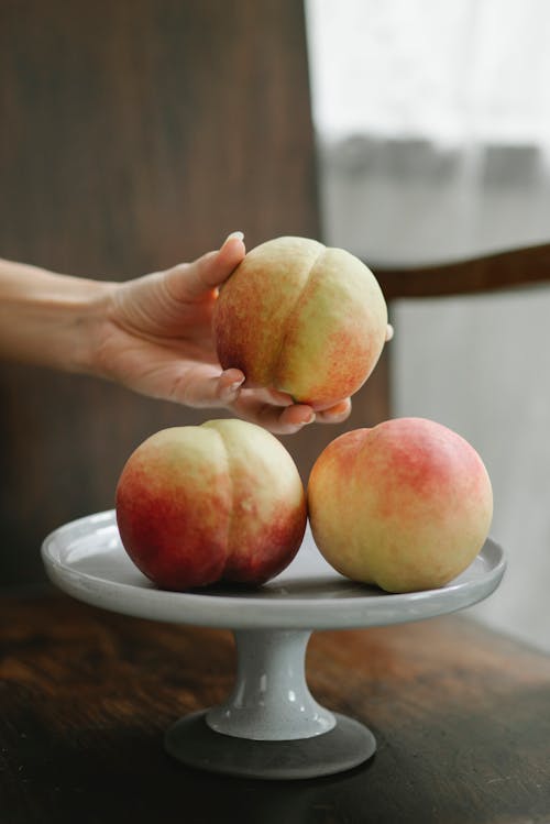 Unrecognizable woman taking fresh juicy ripe peach from white stand on table in kitchen