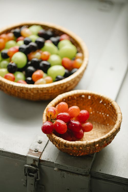 High angle of wicker bowls with fresh blueberries and green and red grapes