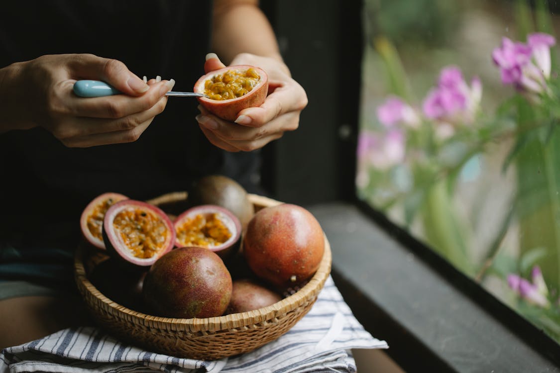 Unrecognizable woman picking up juicy pulp of passion fruit while cooking healthy lunch