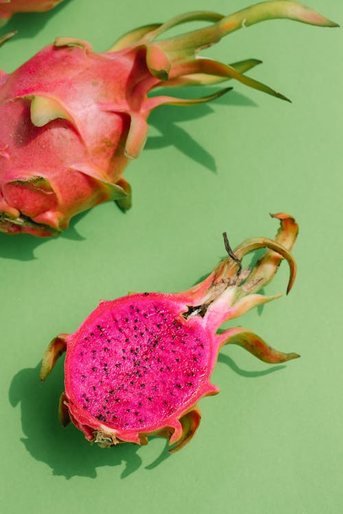 Overhead of bright pink slice of dragon fruit and part of whole fruit placed on green smooth surface