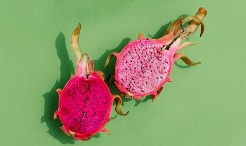 From above of fresh ripe dragon fruit cut in halves casting shadows placed on light green background