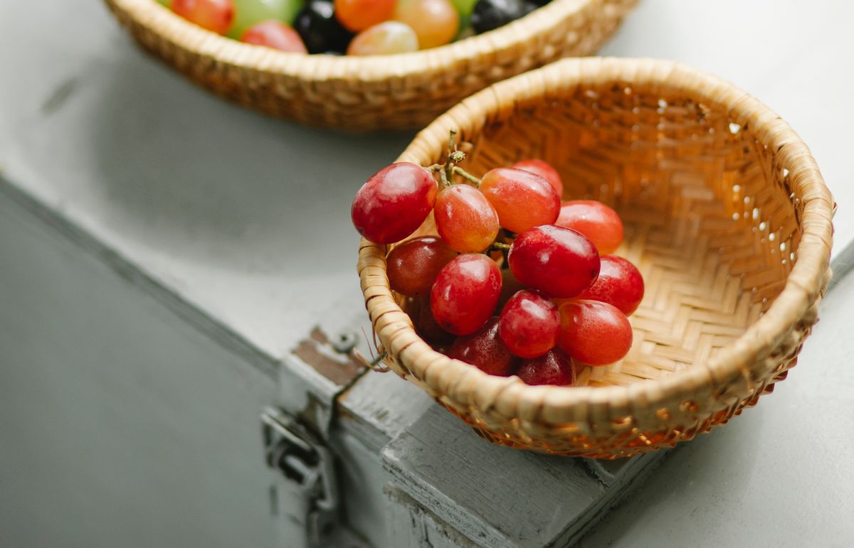 A bowl of fresh green grapes with water droplets on a light wooden table.