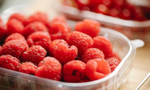 Appetizing red ripe raspberries in small plastic container placed on wooden surface in daylight