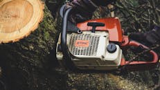 户外，一个人正用电锯切割树干，展示林业工作