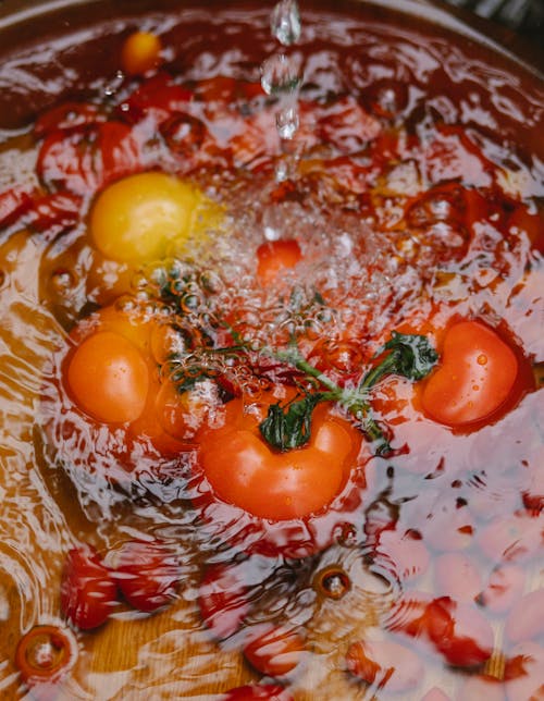 From above of fresh tasty red and yellow peppers placed in bowl in water