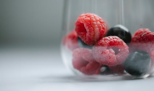Free Closeup of tasty ripe raspberry with blueberry lying in glass on gray background Stock Photo