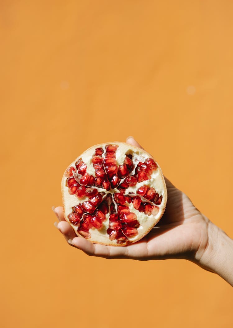 Crop Person With Pomegranate On Orange Background