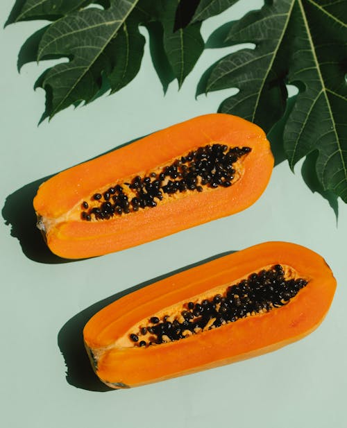 Top view of appetizing composition of ripe papaya with plant leaves on blue background