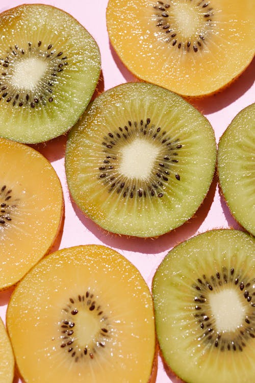 Top view of composed fresh tasty green kiwi slices placed on pink background