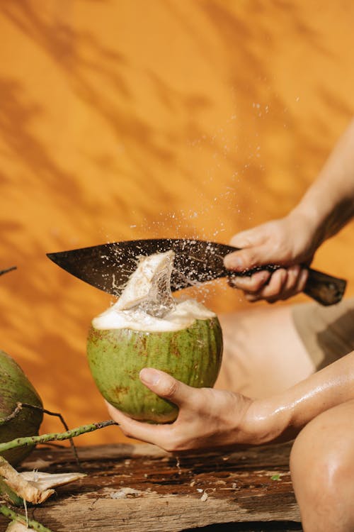 Crop person with knife and green coconut