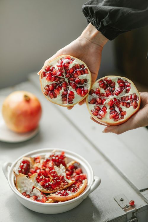 Free From above of crop unrecognizable female with halves and bowl of pomegranate in kitchen Stock Photo