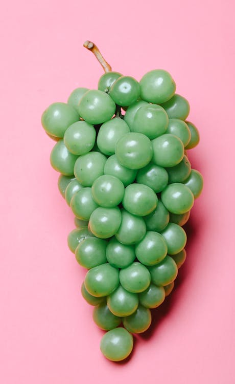 From above of cluster of fresh juicy ripe green grapes placed on pink background