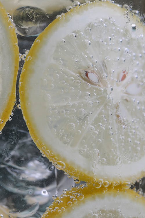 Closeup of sliced unpeeled lemon in transparent glass with ice cubes in beverage