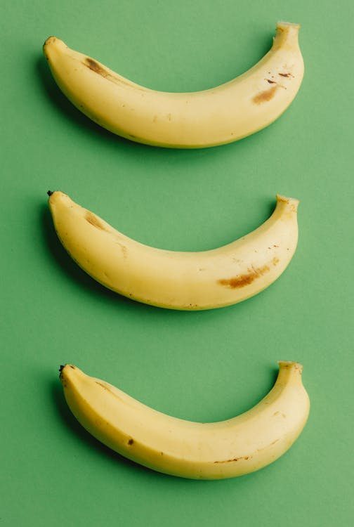 Free Top view composition of healthy ripe bananas with dark spots arranged in row on green background Stock Photo