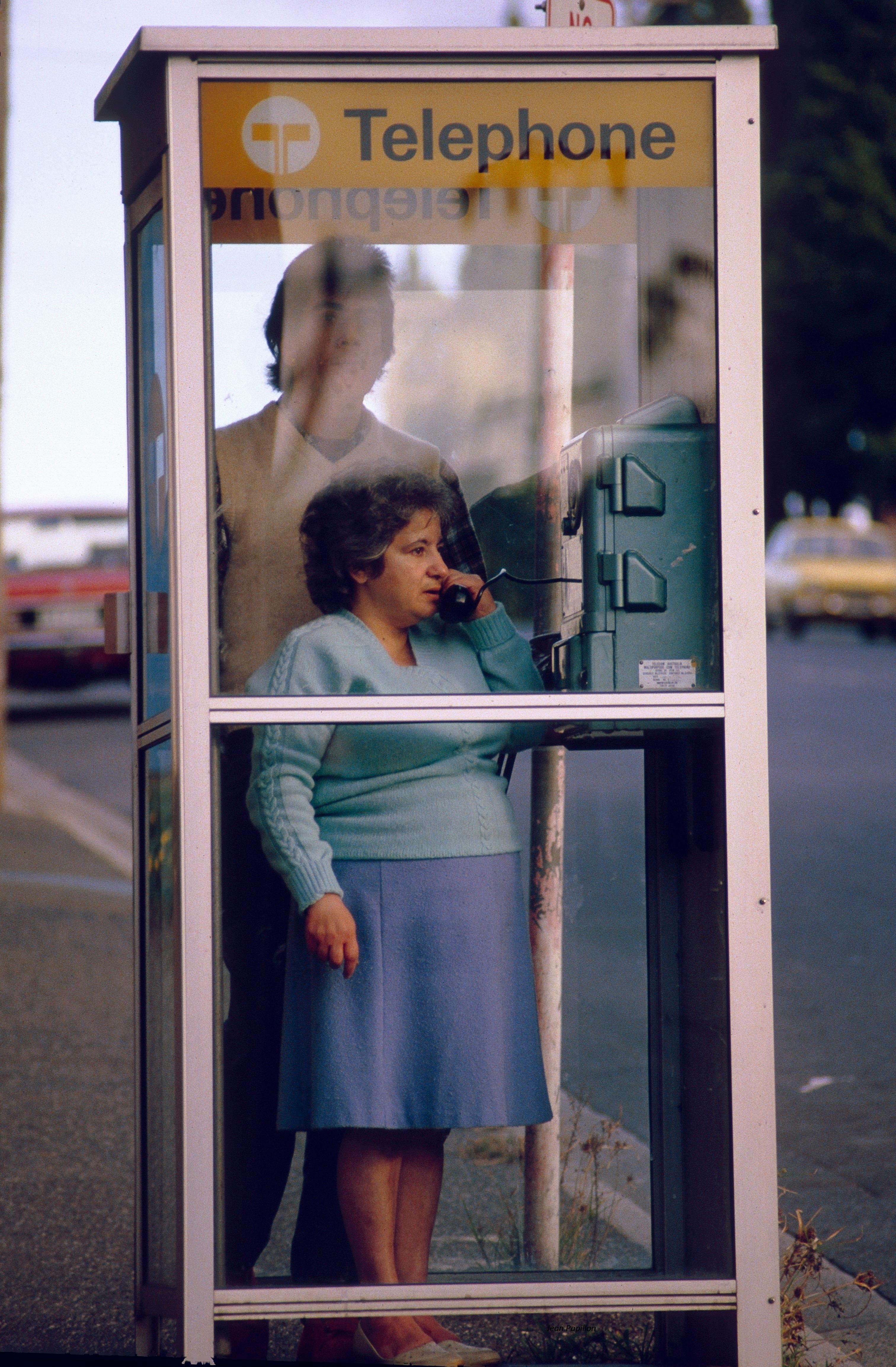 A woman making a call in a vintage telephone booth on a city street, evoking a nostalgic feel.
