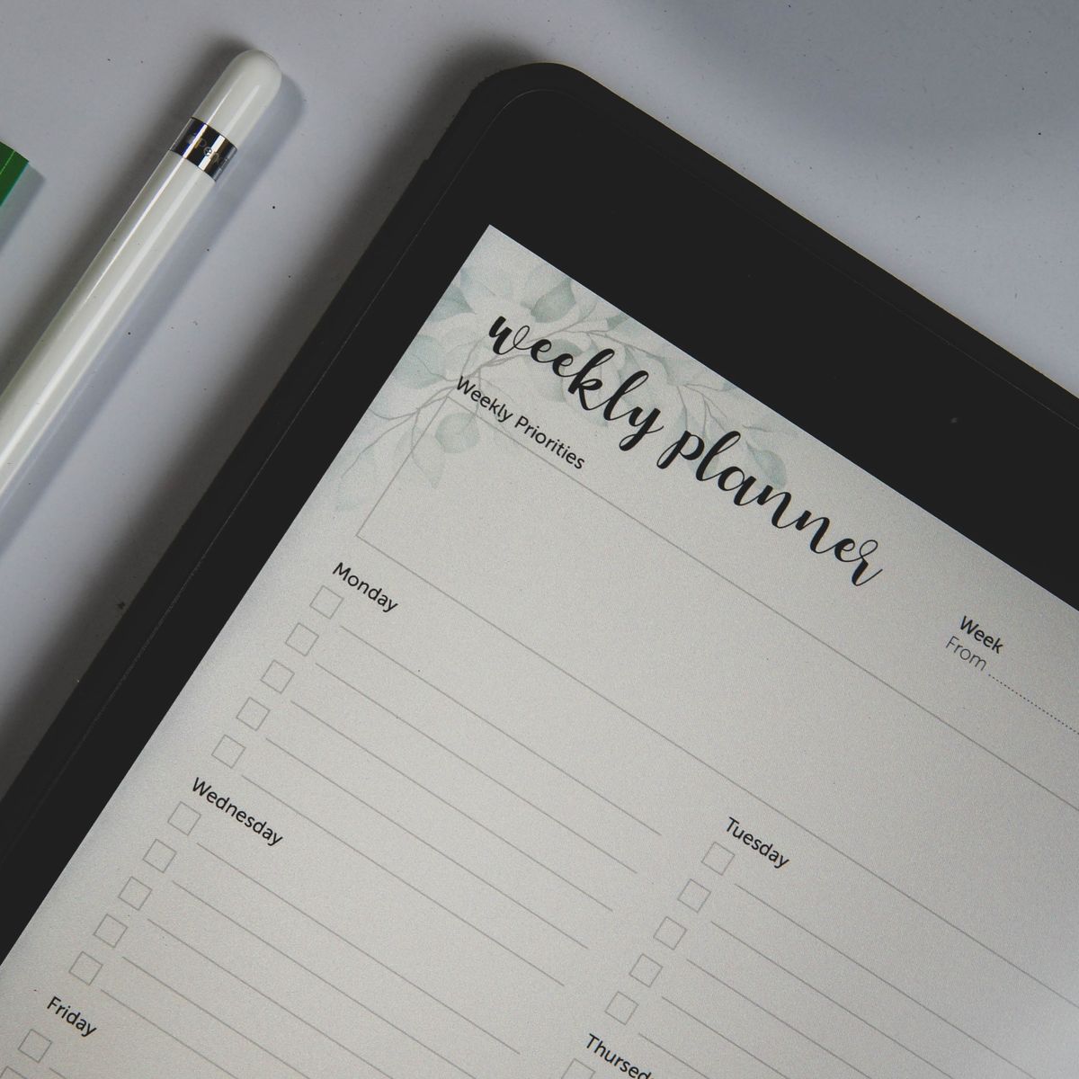 Tablet showing a weekly planner page next to a pen