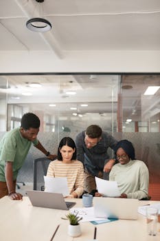 A group of diverse professionals collaborating in a modern office setting, focusing on documents and laptops.