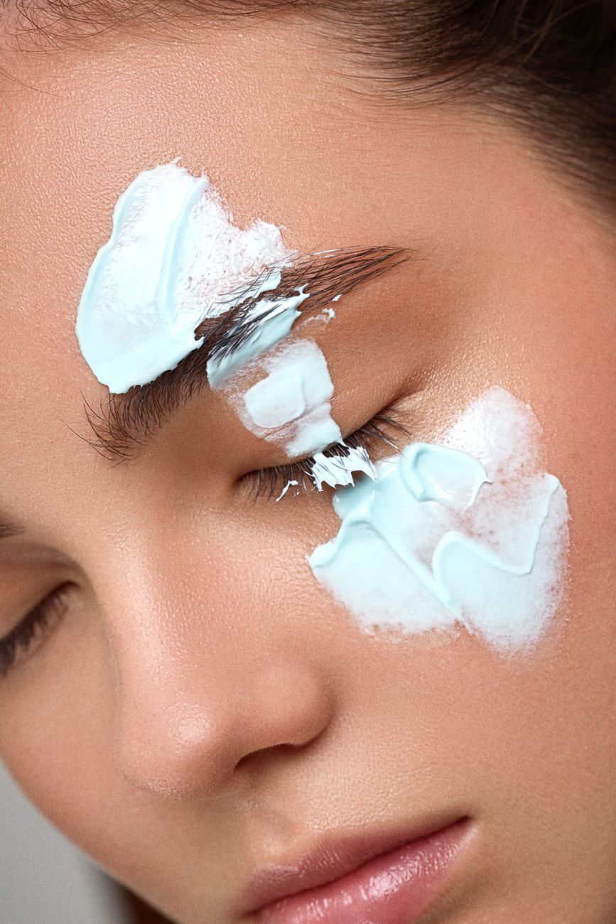 Detailed headshot of a woman applying facial cream, emphasizing skin texture and beauty care routine.
