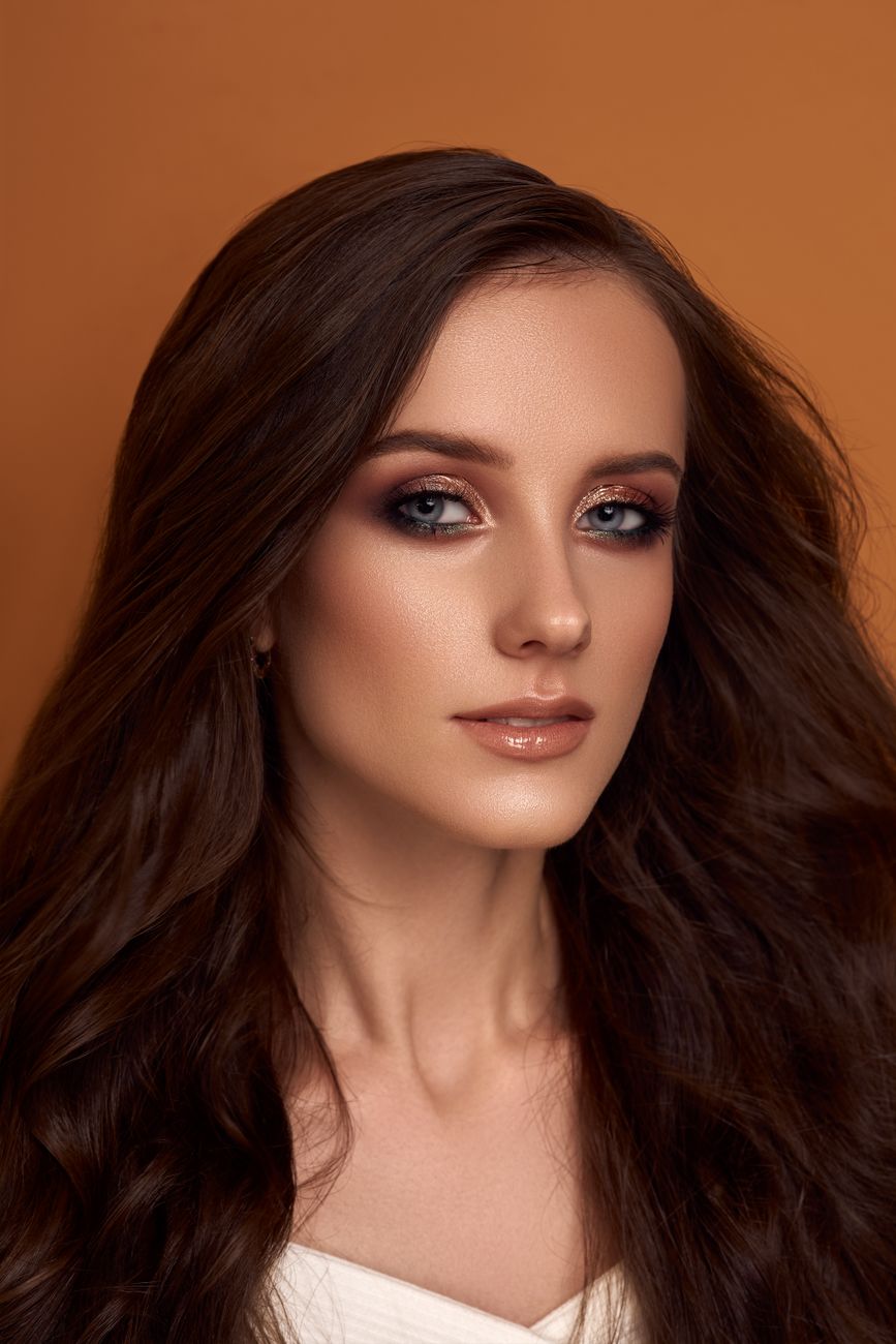 Close-up portrait of a beautiful woman with long hair and makeup against a brown background.