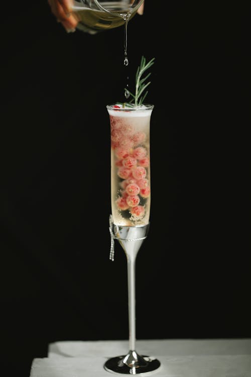 Crop person pouring liquid into crystal flute glass with cocktail and red berries