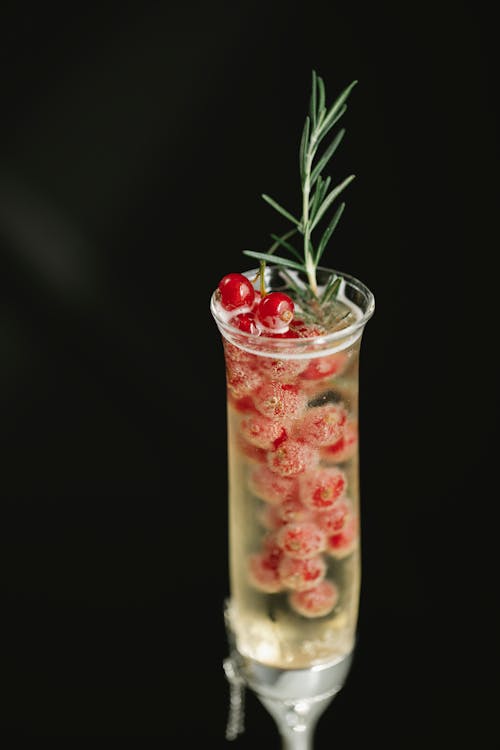 Crystal flute glass filled with alcoholic drink and fresh red berries on black background