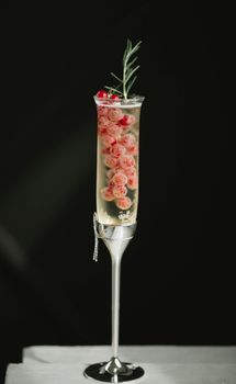 节日鸡尾酒特写：深色背景下，红醋栗与迷迭香在长笛杯中调制而成